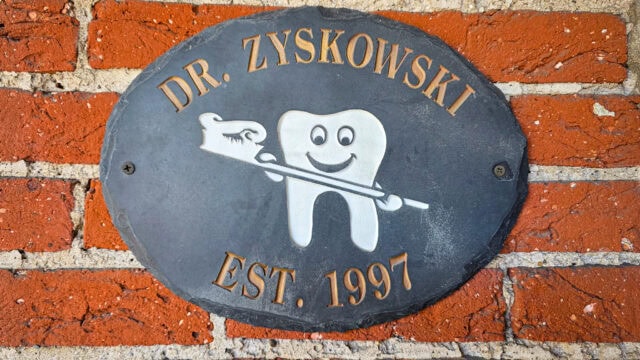 Oval blue plaque on red brick wall reading DR. ZYSKOWSKI EST. 1997 with a tooth illustration and toothbrush.