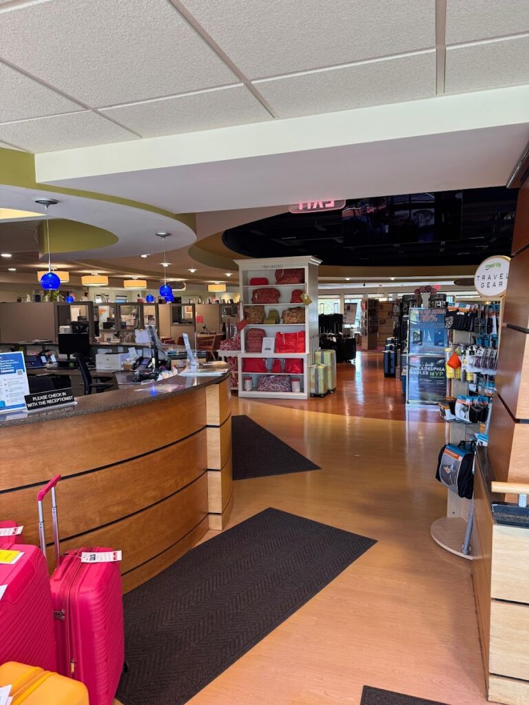 Interior view of a retail store with a curved wooden checkout counter, display shelves, and colorful luggage in a well-lit, modern shopping environment.
