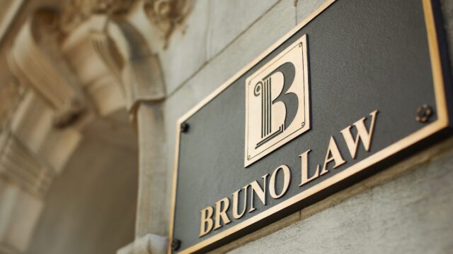 Bruno Law office sign mounted on a building exterior with classic architectural details in the background.