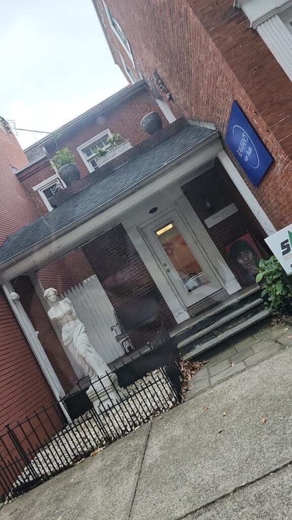 Exterior view of Flavian's, a small brick building with a porch, steps, and a statue outside, located in Easton, featuring a blue sign and potted plants.