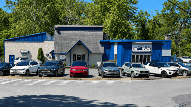 Exterior view of Easton Post automotive service center with multiple cars parked in front, surrounded by green trees and a clear blue sky.
