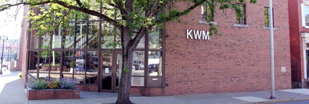 KWM office building with brick exterior and large glass windows, located on a city street with a tree in front.