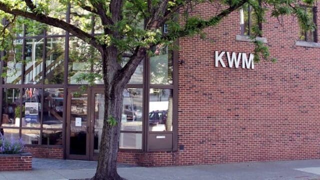 KWM office building with brick exterior and large glass windows, located on a city street with a tree in front.