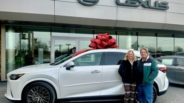 Happy couple standing next to a new white Lexus SUV with a large red bow in front of Lexus of Lehigh Valley dealership.