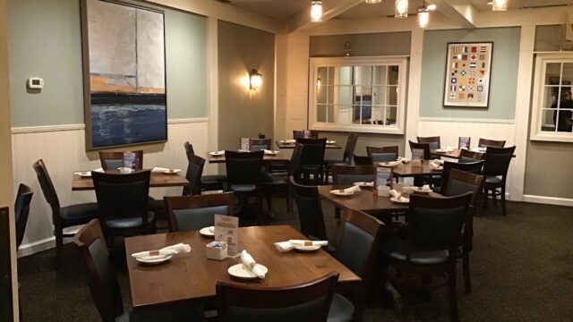Cozy dining area at Marblehead Chowder House with wooden tables, black chairs, and warm lighting, perfect for enjoying seafood and chowder.