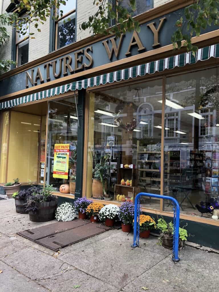 Exterior view of Natures Way Market with colorful flowers and pumpkins outside, showcasing a welcoming storefront on a city street.