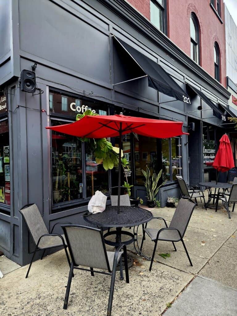 Outdoor seating area at Terra Cafe with a round table, four chairs, a red umbrella, and potted plants outside a black storefront.
