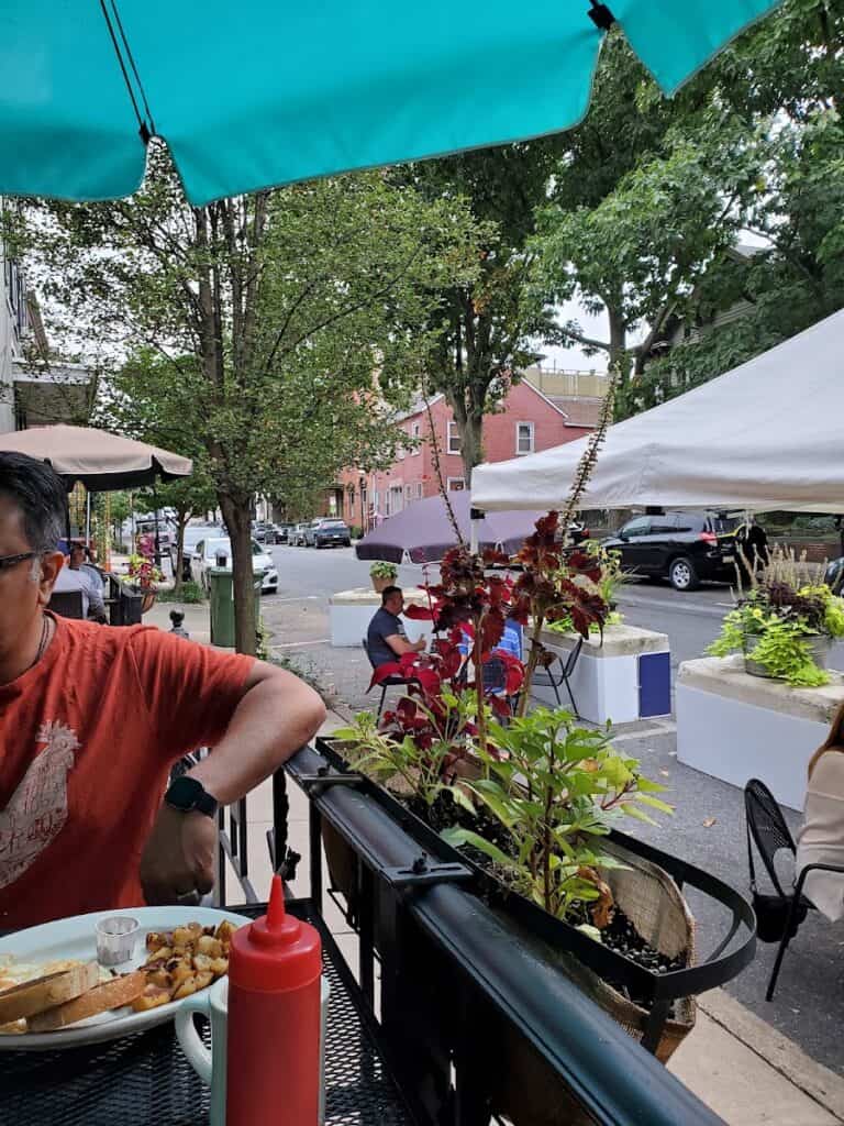 Outdoor dining scene at The State Cafe and Grill with tables, umbrellas, and greenery in a lively street setting.