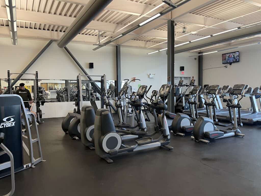 Modern gym with multiple elliptical machines and cardio equipment at Easton YMCA, well-lit with high ceilings and a wall-mounted TV.