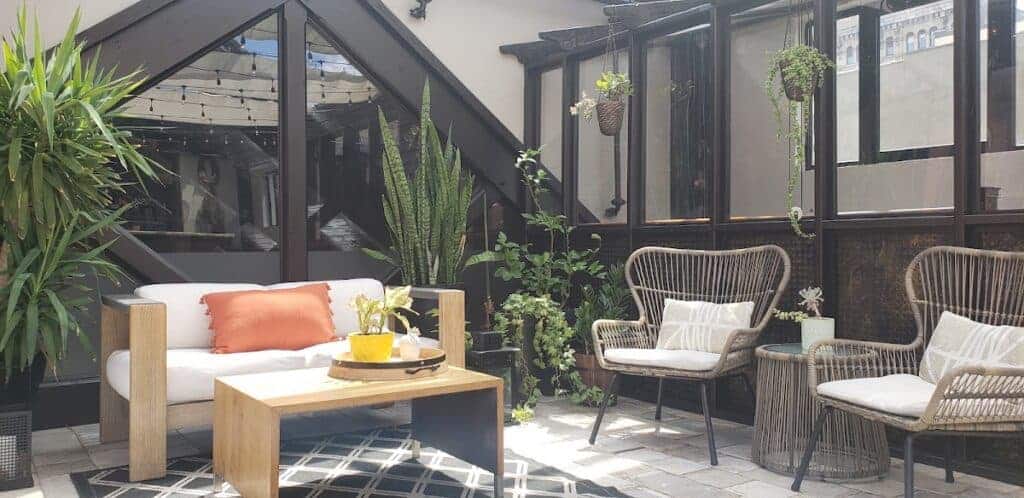 Indoor patio at Easton Post with modern wicker chairs, a white sofa, potted plants, and large windows providing natural light, creating a cozy and stylish atmosphere.