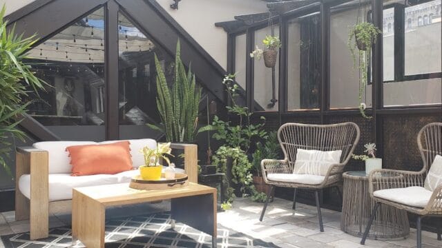 Local Business 12 Indoor patio at Easton Post with modern wicker chairs, a white sofa, potted plants, and large windows providing natural light, creating a cozy and stylish atmosphere.