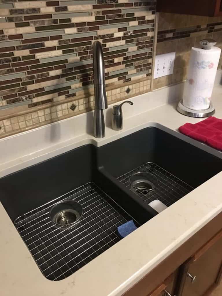 Modern black double kitchen sink with stainless steel grid inserts and a high-arc faucet in a contemporary kitchen setting.