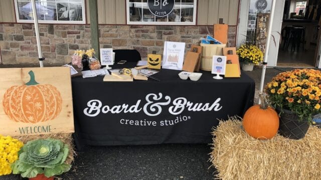 Outdoor display table at Board & Brush Creative Studio in Easton with pumpkins, flowers, and craft supplies for DIY woodworking projects.