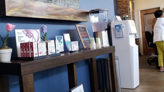 Interior view of Hand & Stone Massage and Facial Spa reception area with water dispenser, promotional materials, and a staff member in the background.