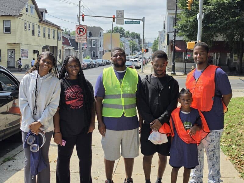 Group of volunteers participating in West Ward Fall Clean-Up Day, wearing safety vests and holding trash bags on a city street.
