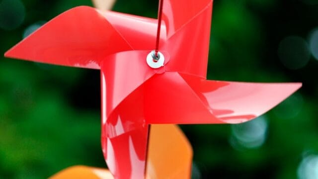 Colorful pinwheels in red and orange spinning outdoors with a blurred green background, symbolizing playful outdoor decor.