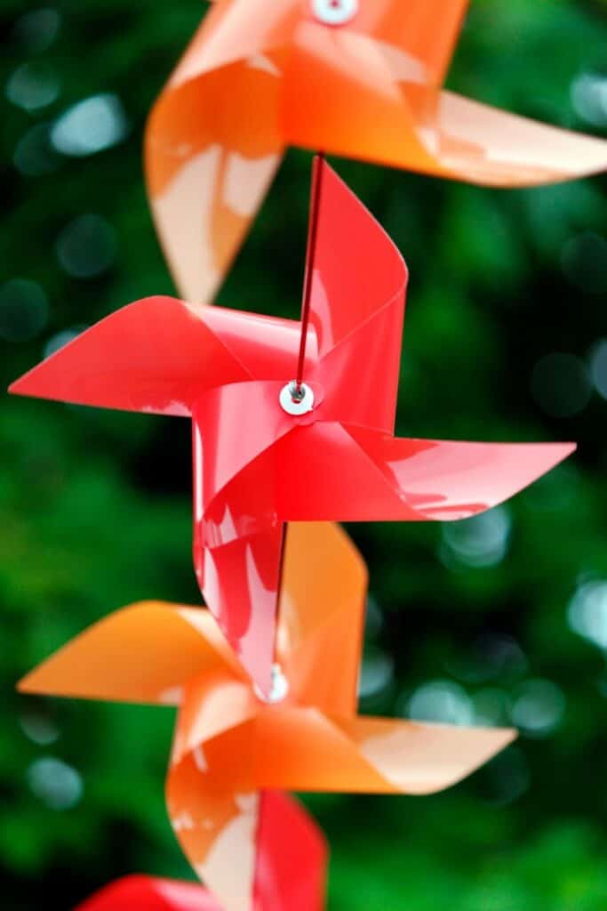 Colorful pinwheels in red and orange spinning outdoors with a blurred green background, symbolizing playful outdoor decor.