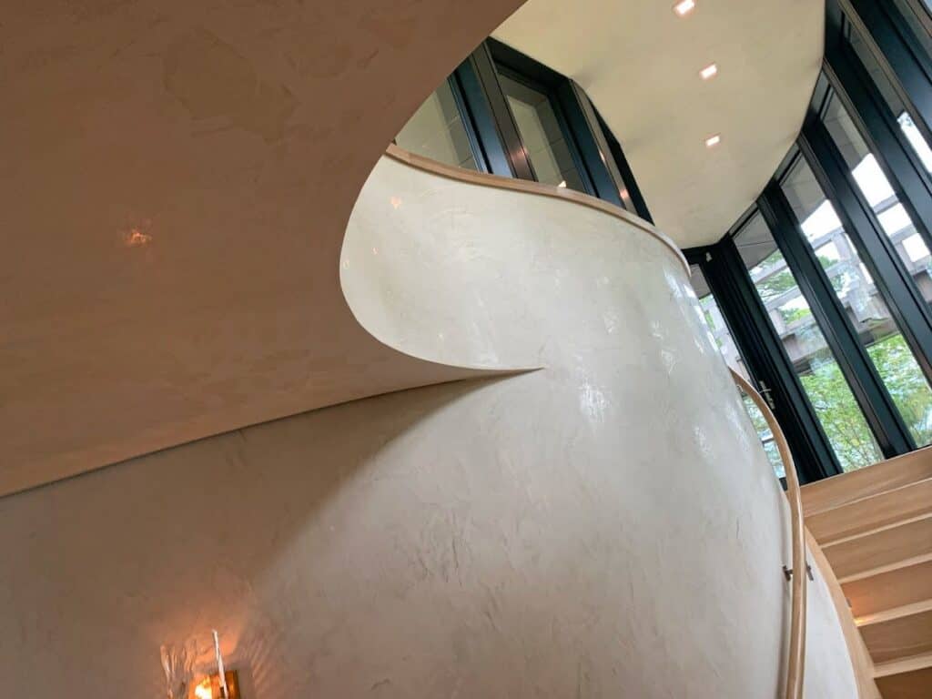 Modern interior staircase with curved white wall and large glass windows in a contemporary building.
