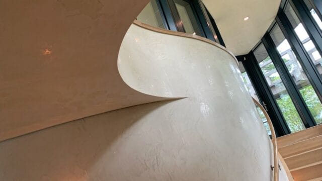 Modern interior staircase with curved white wall and large glass windows in a contemporary building.