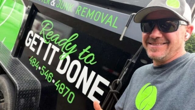 A smiling man in sunglasses and a cap giving a thumbs-up next to a junk removal truck with green and black branding, promoting decluttering and junk removal services.
