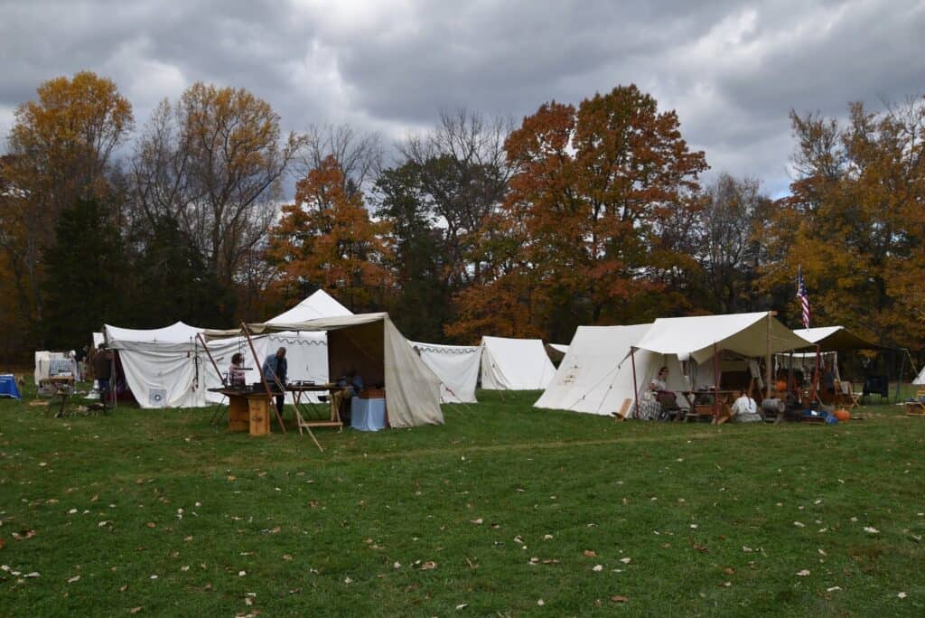 Historical reenactment tents at Market Faire and Rendezvous event with autumn trees and cloudy sky in the background.