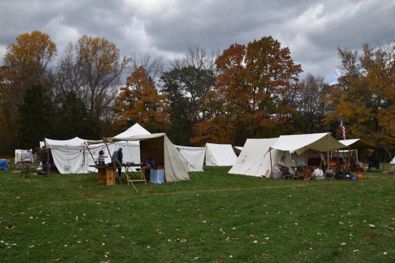 Historical reenactment tents at Market Faire and Rendezvous event with autumn trees and cloudy sky in the background.
